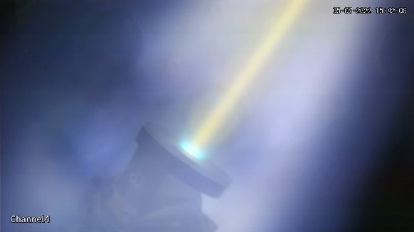 Misty image of a yellow colored plasma beam that turns more cyan colored upon hitting a tungsten target.